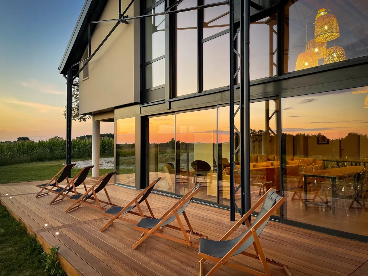 La terrasse en bois de La Maison Welcome et ses transats face à la nature, au crépuscule.
